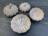 trois citrouilles en métal argenté posées les unes à côté des autres sur une table en bois