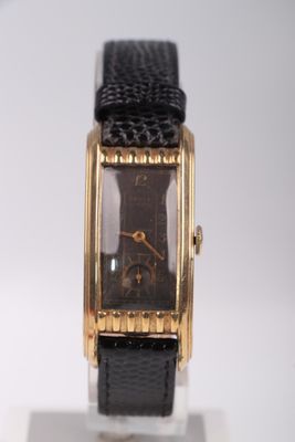 une montre en or avec un bracelet en cuir noir posée sur un fond blanc