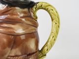 a brown and yellow pitcher with a black handle on a white surface