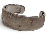 silver cuff bracelet with pink stones on it on a white surface