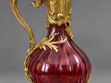 an antique red glass pitcher with gold accents on a stand