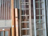 une échelle appuyée contre un mur, à côté d'un tas de vieilles fenêtres