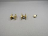 two gold tie pins and a pearl on a white surface