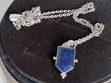 un collier orné d'une pierre bleue, présenté dans un coffret noir