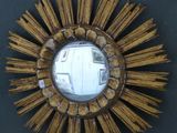 a gold starburst mirror on the wall next to a black wall