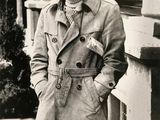 black and white photo of a man in a trench coat standing on a sidewalk