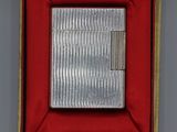 un vieux briquet en argent dans une boîte rouge posée sur une table