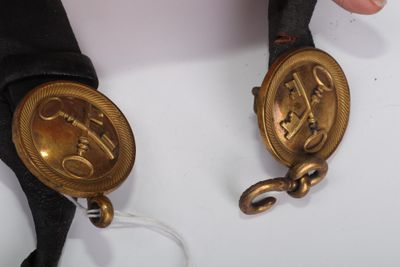 Quelqu'un tient une paire de ceintures noires et dorées ornées d'un cheval.