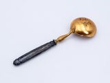 an antique gold spoon with a black handle on a white surface