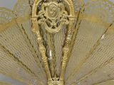 gold metal fan with ornate design on top of it on a white surface