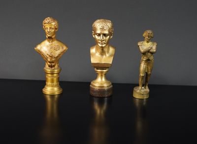 trois busturines dorées posées sur une table noire, sur fond gris