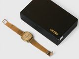 a gold watch sitting next to a black box on a white surface