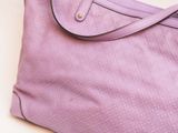 purple handbag with strap on white surface with white background