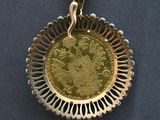 a gold coin in the middle of a necklace on a black background