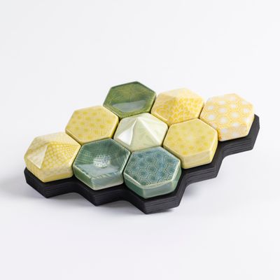 des hexagones en céramique jaunes et verts disposés sur un plateau noir, sur fond blanc