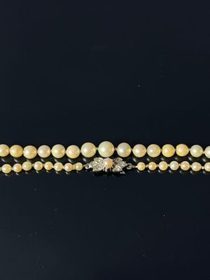 a close up of a necklace with pearls and diamonds on a black surface