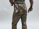bronze statue of a boy standing on a rock with his hands on his hips