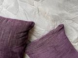 two purple pillows on a white bed with a white comforter
