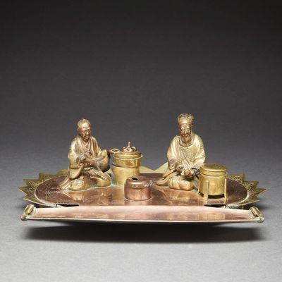 bronze figurines of two men sitting on a tray with a bowl of food