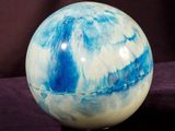 a blue and white marble ball sitting on a black surface