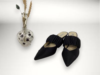 une paire de chaussures noires à bout pointu à côté d'un vase de fleurs