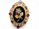 une broche noire et dorée ornée d'une fleur entourée de saphirs roses