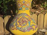 brightly colored vase sitting in front of a wooden fence in a garden