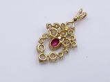 a close up of a gold plated pendant with a red stone