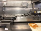 stainless steel counter top in a commercial kitchen with a pizza on a cutting board