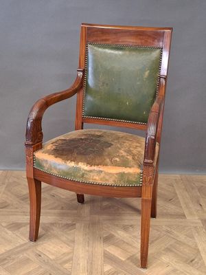 une vieille chaise en bois recouverte de cuir vert, posée sur un parquet