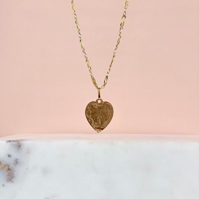 un collier avec un cœur en or et une chaîne, sur fond rose