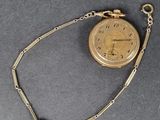 une montre de poche en or, suspendue à une chaîne, posée sur une table