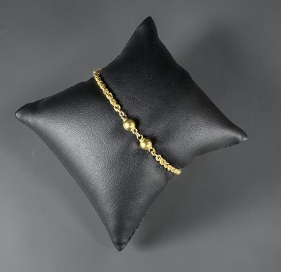 a black pillow with a gold beaded bracelet on it