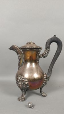 silver plated coffee pot with ornate decoration on stand on grey background