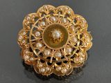 a gold brooch with pearls in it on a black surface