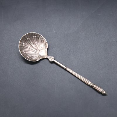 a silver spoon with a shell shaped handle on a black surface