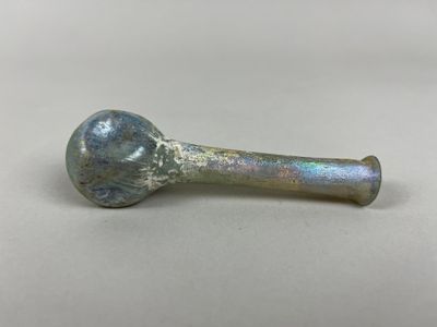 une vieille pipe en verre munie d'un manche en métal, posée sur une surface blanche