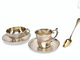deux tasses et soucoupes en argent, accompagnées de cuillères, posées l’une à côté de l’autre