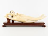 une figurine en ivoire représentant une femme allongée, posée sur un socle en bois