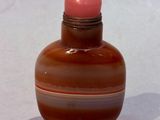 a small glass bottle with a pink top on a white surface