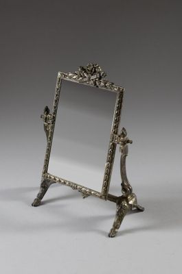 un miroir ancien plaqué argent, posé sur un pied et orné d'un oiseau