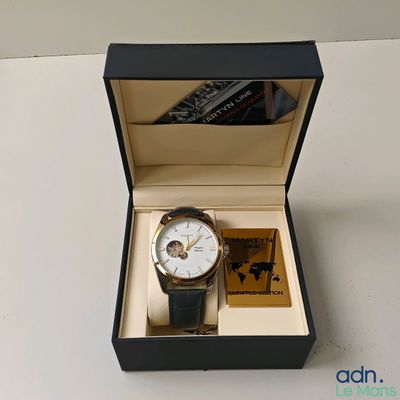 une montre dans une boîte posée sur une table, à côté d'un livre