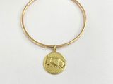 un bracelet rigide en or orné d'une breloque en forme de pièce de monnaie