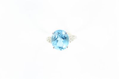 une bague avec une topaze bleue ovale et des diamants, sur fond blanc
