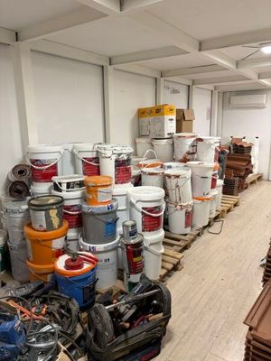 de nombreux seaux de peinture posés sur des palettes dans une pièce