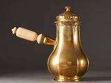 an antique brass coffee pot with a wooden handle on a gray surface