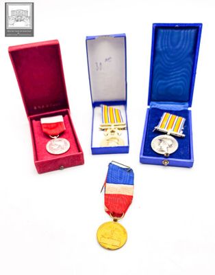 trois médailles et une médaille dans un écrin rouge posé sur un fond blanc