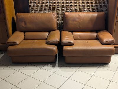 une paire de fauteuils inclinables en cuir marron avec des repose-pieds assortis dans un salon