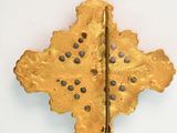 brass cross with holes in the middle on a white surface