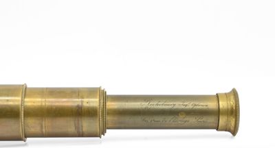 un télescope ancien en laiton posé sur une surface blanche, avec un fond blanc